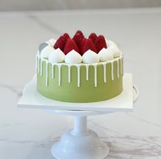 a green cake with white icing and strawberries on top