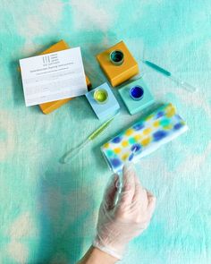 a person in white gloves is holding up some items on a blue surface with green and yellow colors