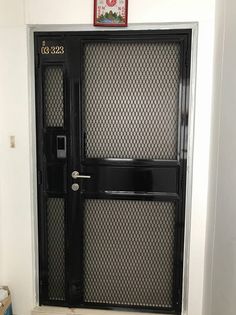 a black door with metal mesh panels and numbers on the top panel is in front of a white wall