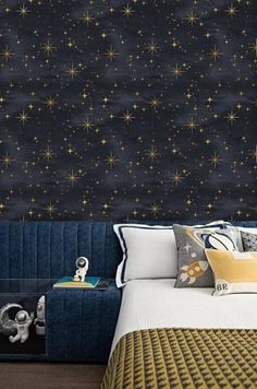 a bed sitting under a night sky with stars painted on the wall and pillows in front of it