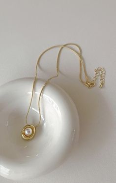 a white bowl with a gold necklace on it's neck and a chain hanging from the side