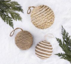 three woven ornaments sitting in the snow next to evergreen branches and twine wrapped around them