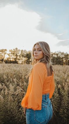 a woman standing in a field with her back to the camera and looking off into the distance