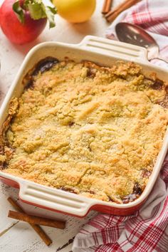 a casserole dish with apples, cinnamon sticks and an apple in the background