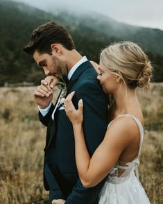 a bride and groom standing in the middle of an open field with mountains in the background