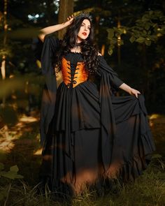 a woman in a black and orange dress standing in the woods with her hands on her head