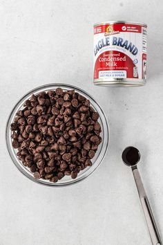 chocolate chips in a glass bowl next to a can of milk and spoon on a white surface