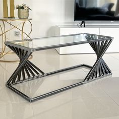 a glass and metal coffee table in front of a flat screen tv on a stand