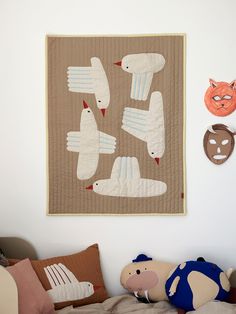 stuffed animals are sitting on the bed in front of a quilted animal wall hanging