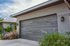 a garage door is open in front of a house with plants and shrubs around it