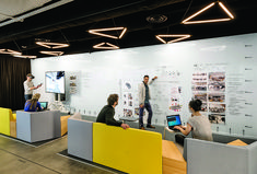 people are sitting at desks with laptops and papers on the wall behind them