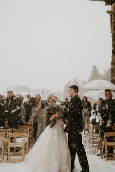 a bride and groom are standing under an umbrella in the snow at their wedding ceremony