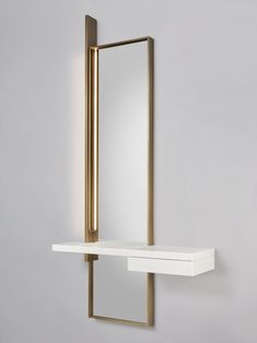 a white shelf with a mirror on it and a gold frame around the edge, against a gray wall