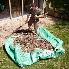 a man is shoveling wood into a pile in the yard with a green tarp