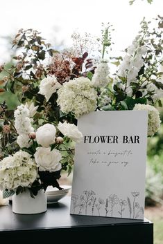 white flowers are in vases next to a flower bar sign