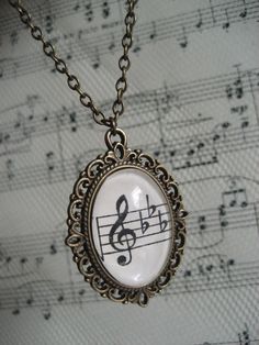 a necklace with musical notes on it sitting on top of sheet music notations in black and white