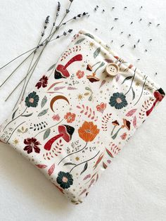 a white cloth covered with flowers and plants on top of a table next to some knitting needles