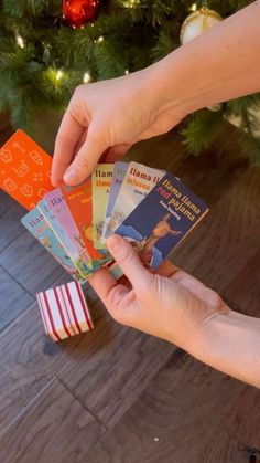 a person is holding several cards in front of a christmas tree