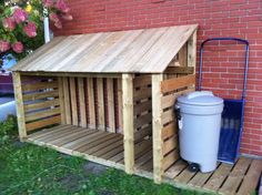 a dog house made out of pallets and wooden slats with a trash can next to it