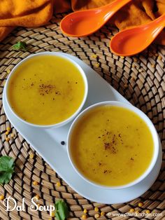 two bowls of soup sit on a wicker place mat with spoons next to it