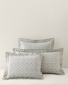 three pillows on a white bed with blue and green floral print, one has a scalloped edge