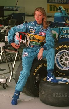 a woman sitting on top of a tire next to a race car in a garage