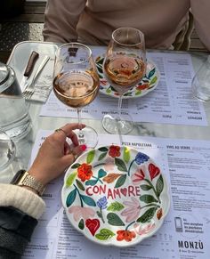 a woman sitting at a table with two wine glasses and a plate that says conamare