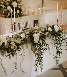 the table is set with white flowers and greenery, candles and napkins on it