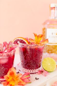 two glasses filled with red liquid and garnished with oranges, flowers and lemon slices