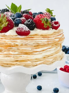 a stack of pancakes topped with berries and powdered sugar on a white cake plate