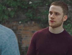 a man in a red shirt is standing next to another man wearing a blue sweater