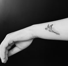 a small bird tattoo on the left inner forearm and wristband is shown in black and white