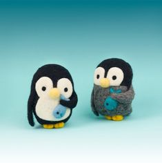 two small stuffed penguins sitting next to each other on a light blue background, one holding a baby penguin