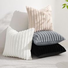 three pillows stacked on top of each other in front of a white wall and plant