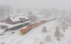 a train traveling through a snow covered rural country side next to a red brick building