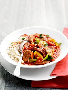 a white bowl filled with meat and vegetables next to rice on top of a red napkin