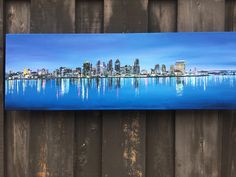 a painting of a city skyline is hanging on a wooden fence in front of a wood paneled wall