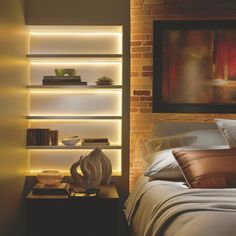 a neatly made bed in front of a brick wall with bookshelves on it