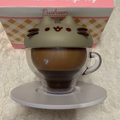 a coffee cup with a cat face on it's head in front of a box