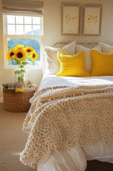 a white bed topped with yellow pillows next to a vase filled with sunflowers