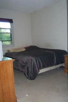 an empty bedroom with a bed, dresser and television in it's corner next to a window