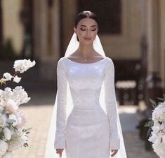 a woman wearing a wedding dress and veil standing in front of white flowers with her hands on her hips