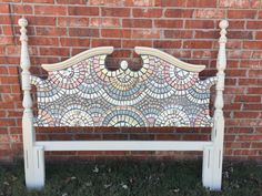 a white bench sitting in front of a brick wall with a mosaic design on it