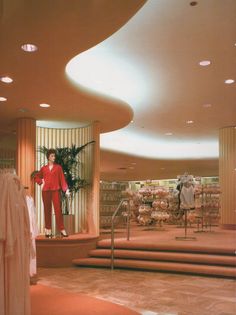 a woman standing in front of a store display with clothing on racks and mannequins