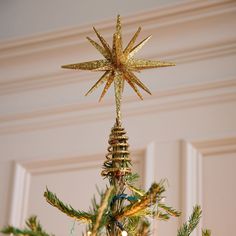 a gold star ornament hanging from the top of a christmas tree