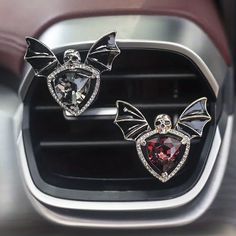 two pairs of earrings on the dashboard of a car, one with wings and diamonds