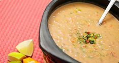 a bowl of soup with a spoon in it on a red place mat next to some fruit