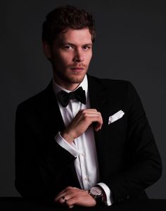 a young man in a tuxedo poses for a photo with his hand on his tie