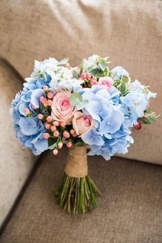 a bouquet of blue and pink flowers sitting on top of a couch next to a pillow