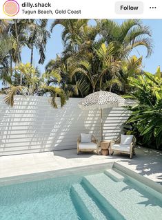 an outdoor swimming pool with two chairs and an umbrella next to the pool is surrounded by palm trees